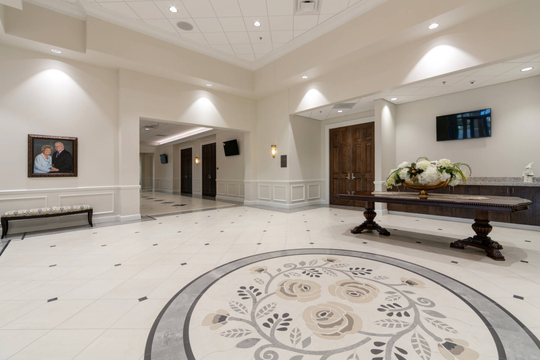 Light-colored premium ceramic tile in an events center common area. The centerpiece is a tile medallion of cream roses and leaves.
