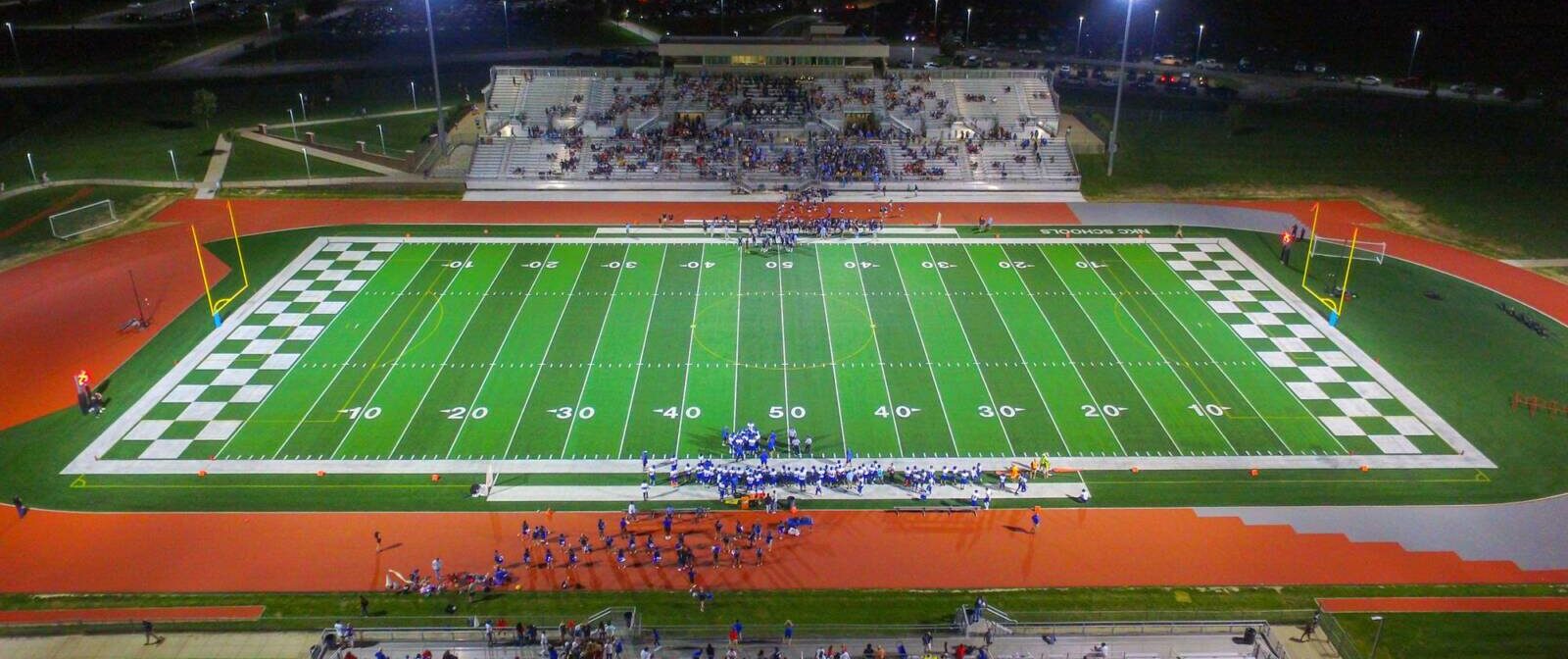 Drone shot of high school football field with checkered end zones corresponding with an orange and gray track