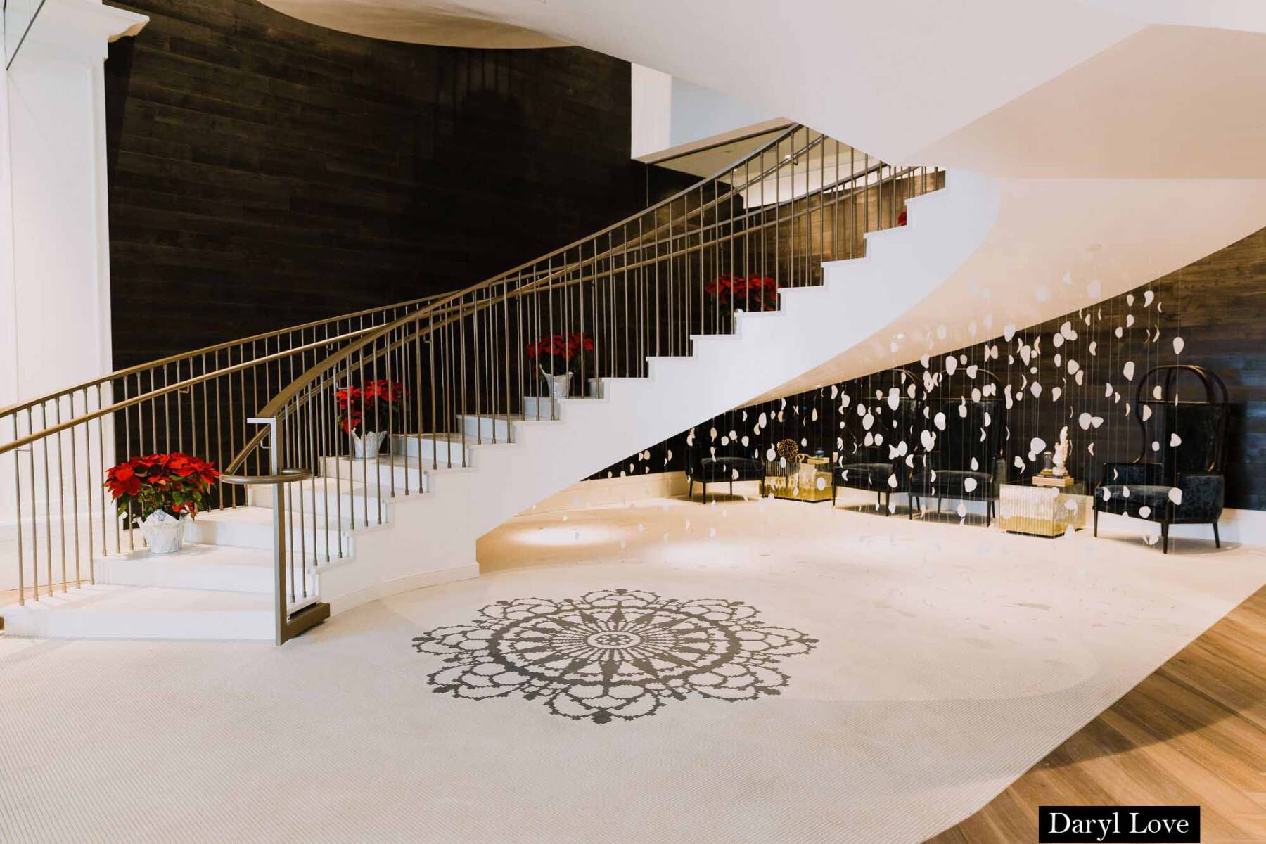 Curving staircase with gold banister leads to a large open space with white flooring and an ornate black medallion.