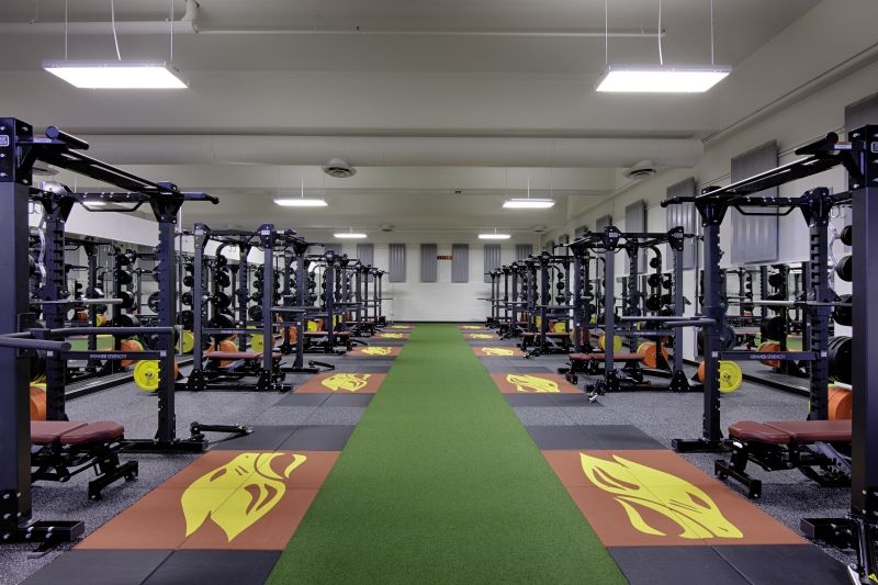 The Concordia University Fitness Center with numerous squat racks on a commercial rubber floor with a green walkway