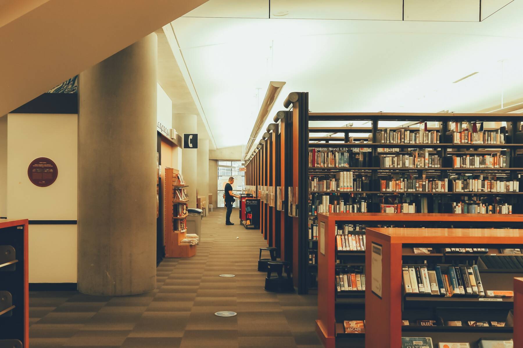 Photo of the library consisting of many book shelves, a phone call area, and a person looking for books