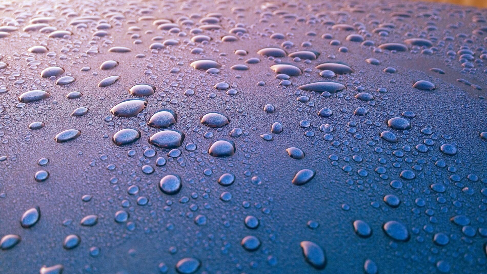 A stock image of circular water droplets on a dark, purple-like ground