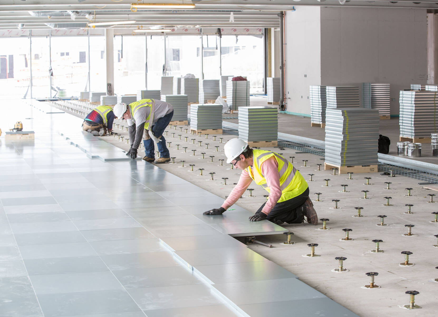 Three workers in the process of installing gray, raised flooring with many tiles to be used behind them